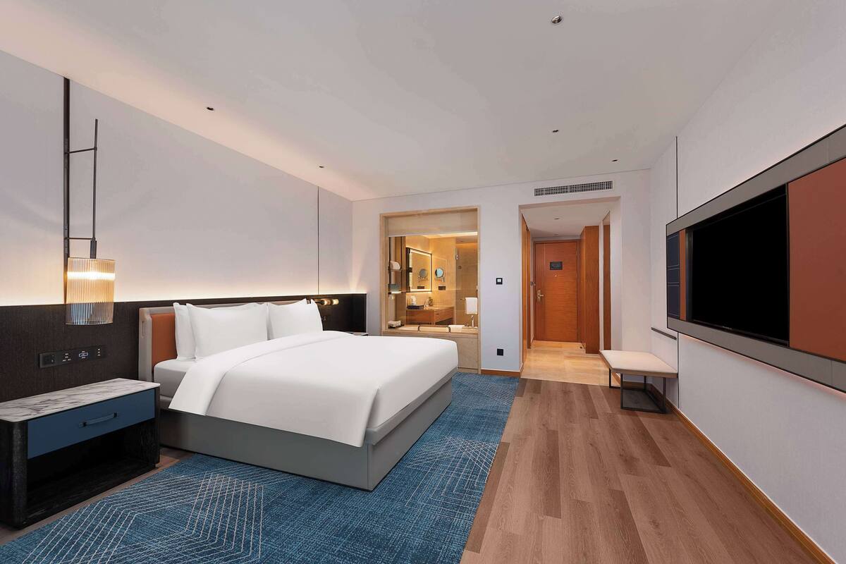 Una habitación de hotel moderna con una cama grande, un escritorio, un televisor y un baño visible a través de una puerta abierta.
