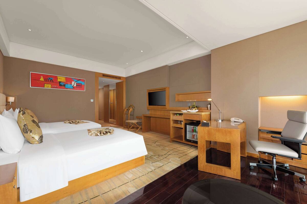 Una habitación de hotel con cama, escritorio, silla, televisión y un cuadro en la pared.