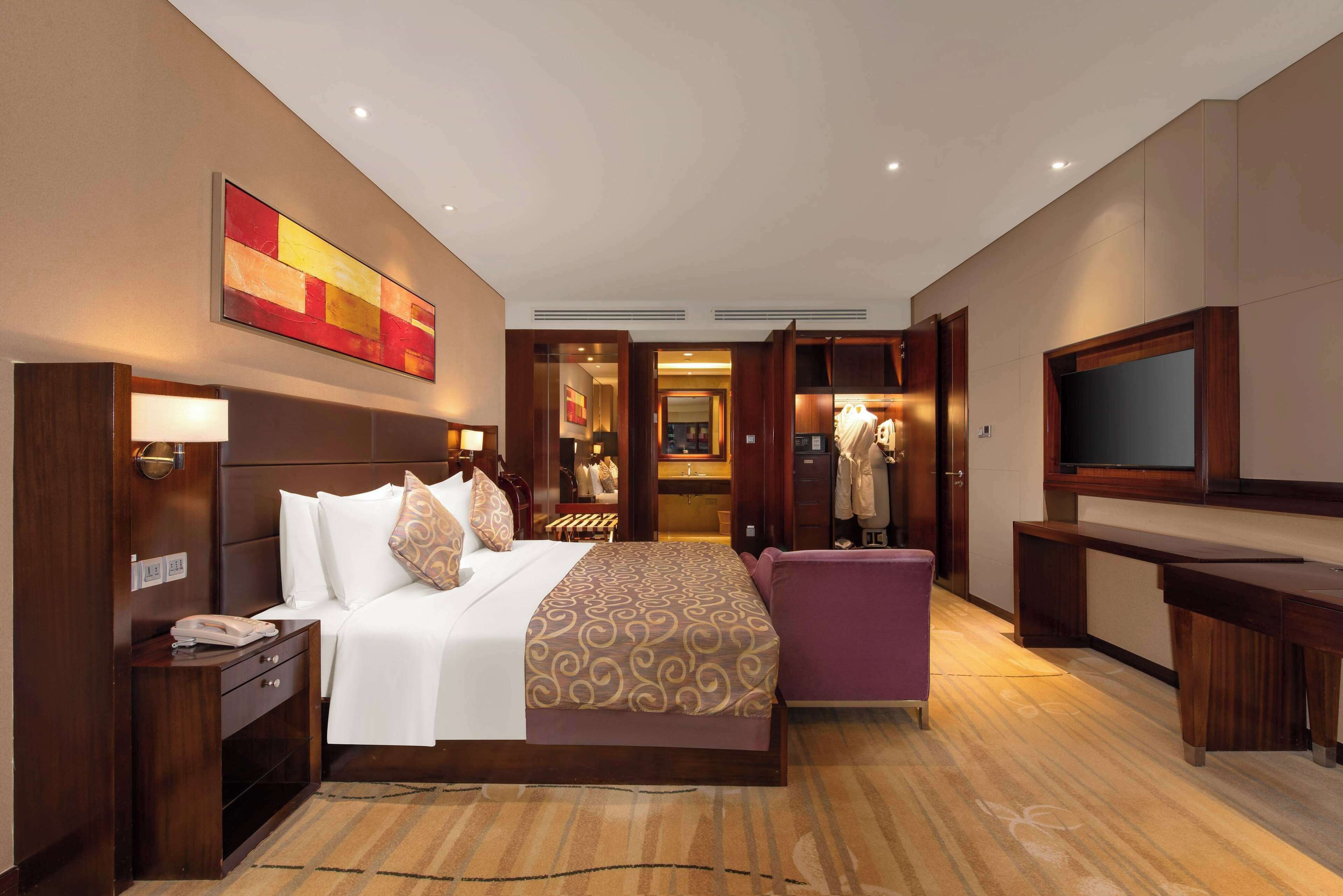 Habitación de hotel con una cama grande, un escritorio, una silla, un televisor y un baño visible a través de una puerta abierta.
