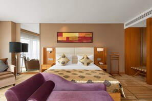 A hotel room with a large bed, two bedside tables, a chair, a floor lamp, and a wooden wardrobe.