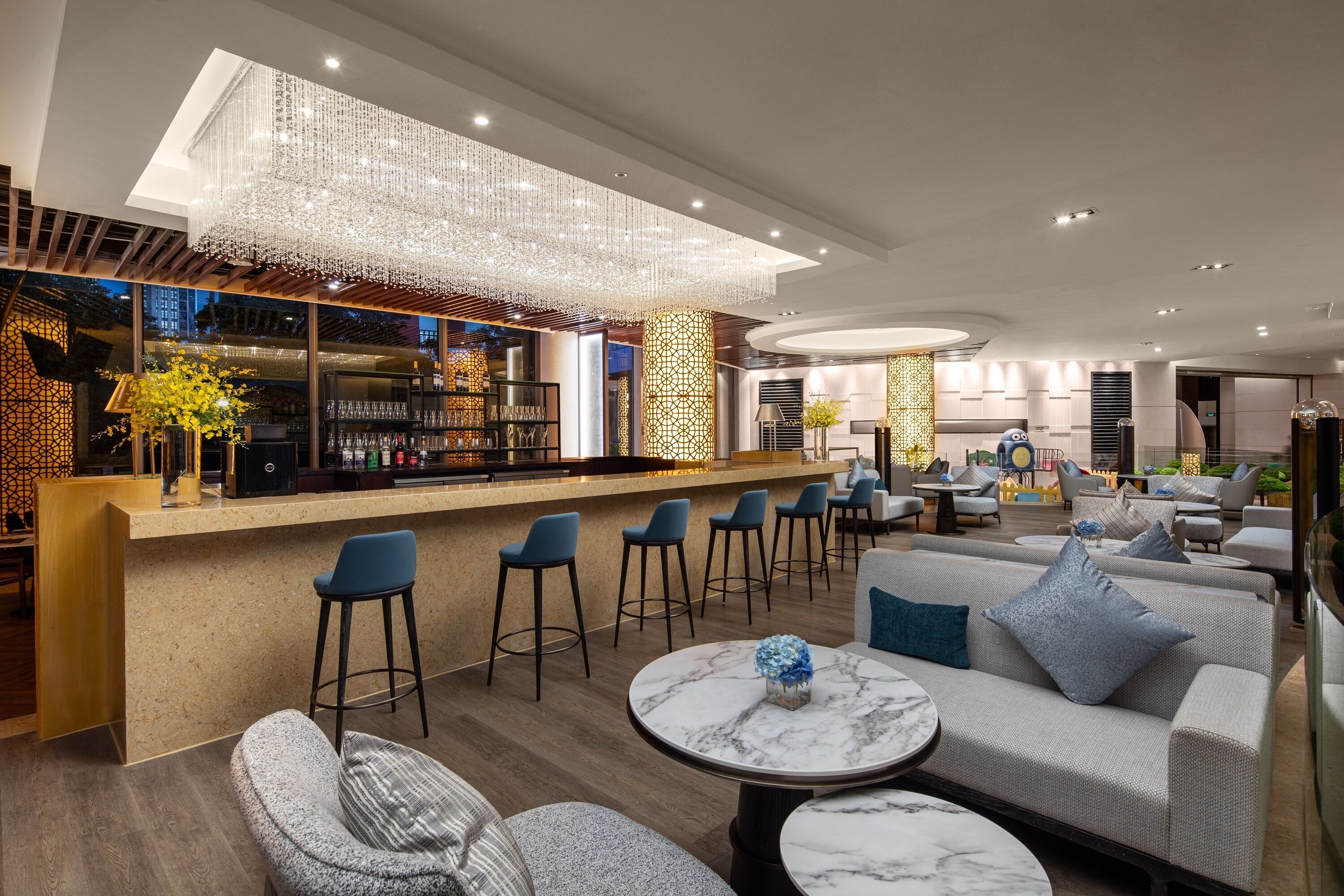 A modern bar area with a high ceiling, bar stools, and a seating area with sofas and round tables.