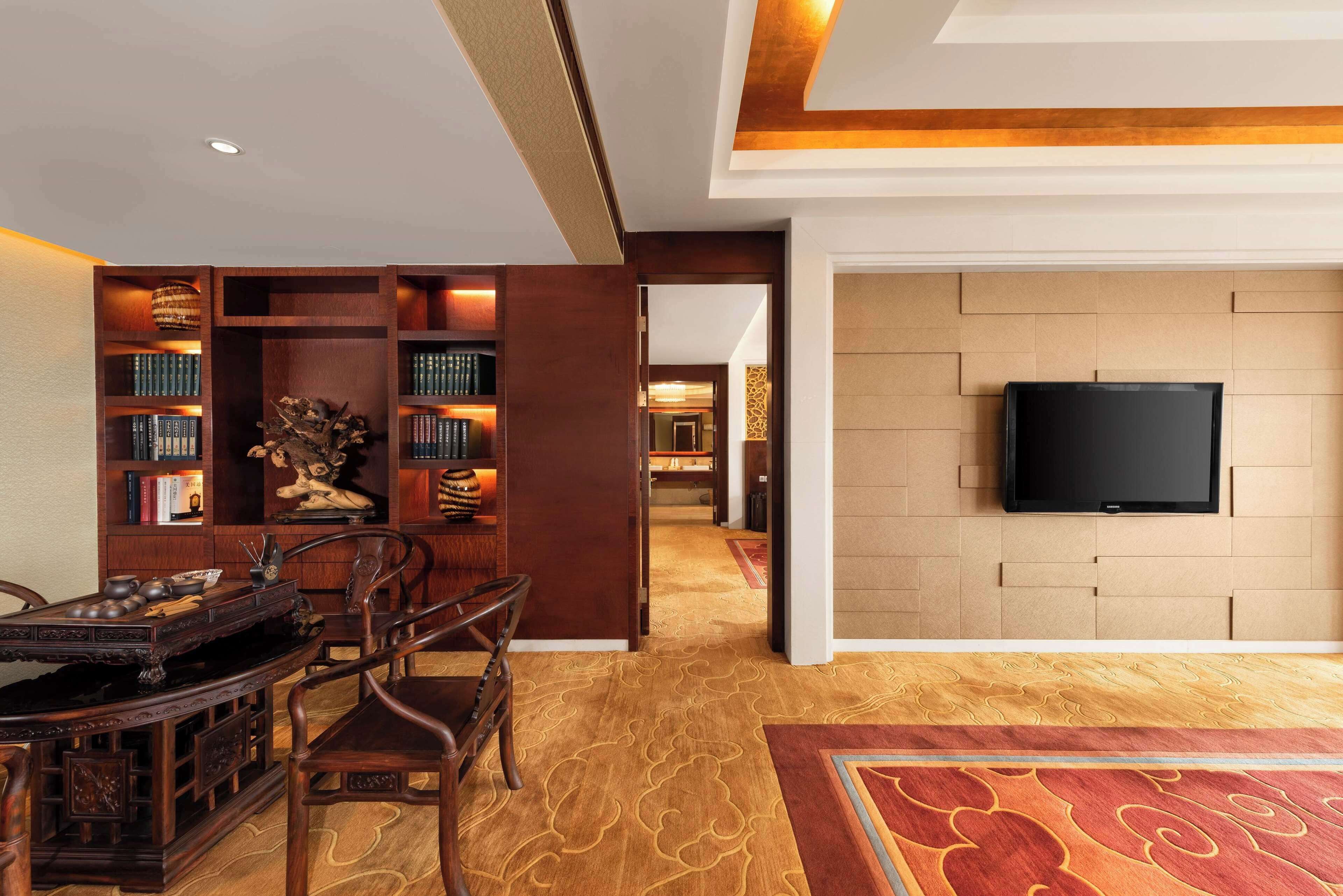 Un salón de estilo tradicional con una estantería de madera, un televisor montado en la pared y una alfombra estampada.