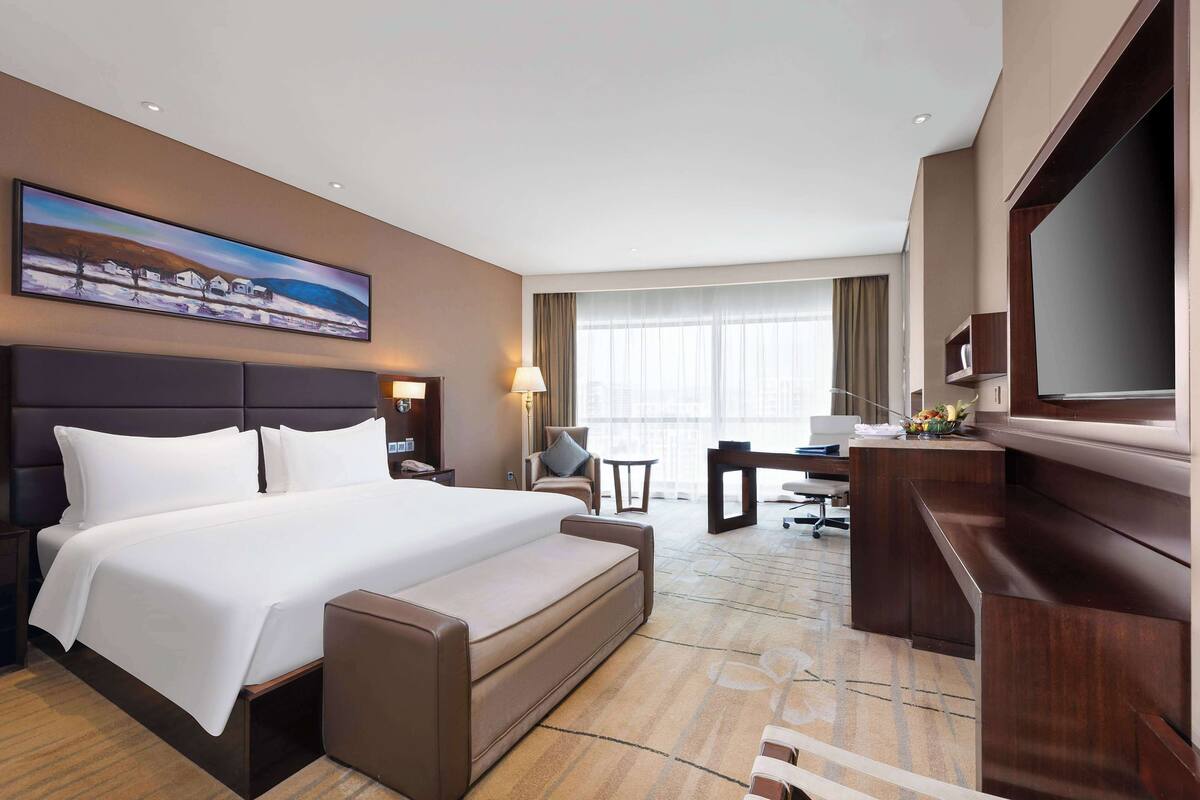 Una habitación de hotel con una cama grande, un escritorio, un sofá, un televisor y un cuadro en la pared.