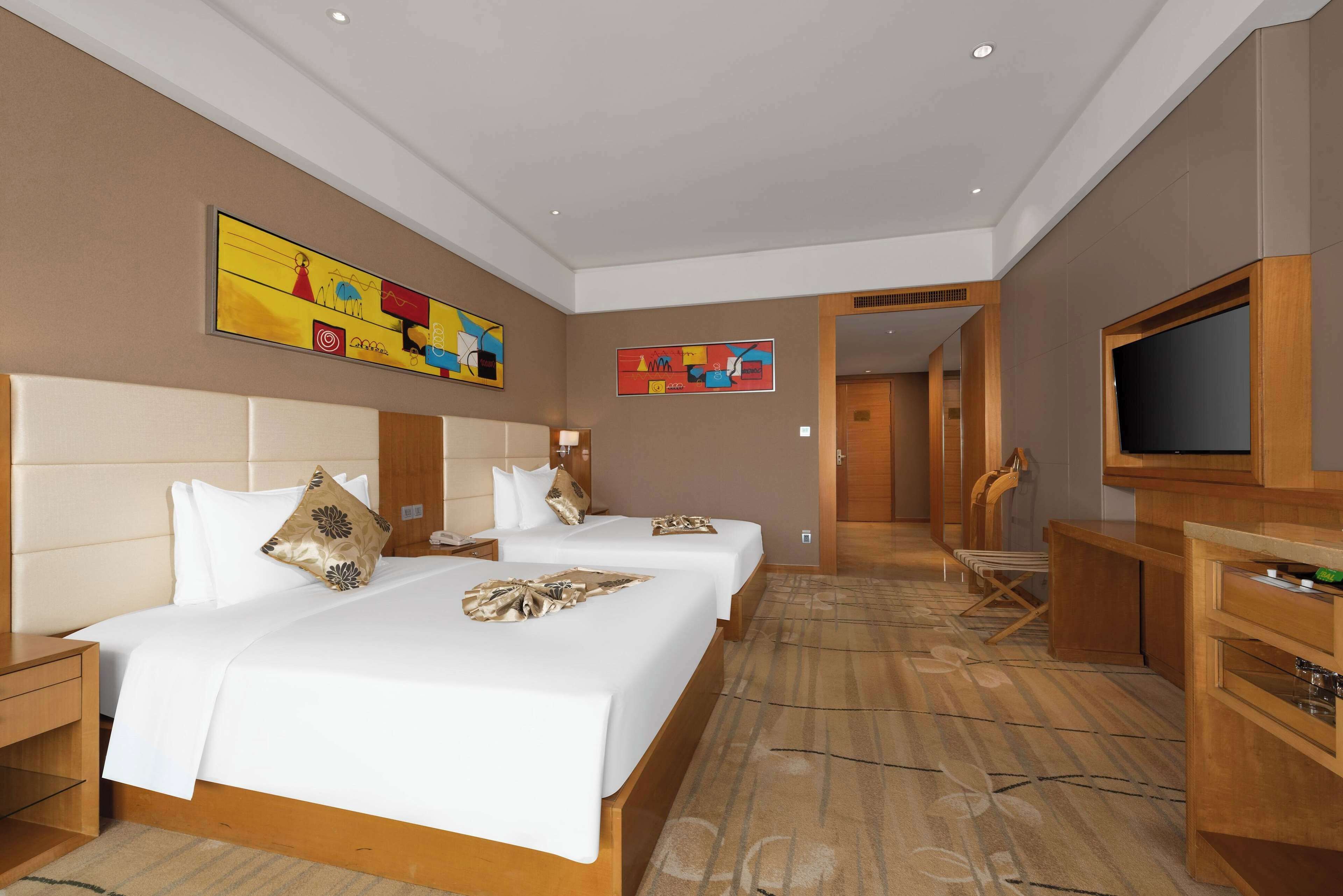 A hotel room with two beds, a TV, and a desk.