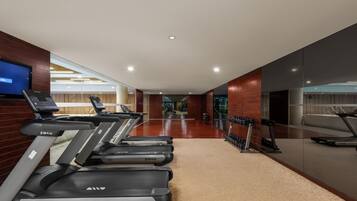 Un gimnasio moderno con cintas de correr, un espejo grande y una pantalla de televisión.