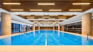 Une piscine intérieure dotée d’un sol carrelé, de poutres en bois au plafond et offrant une vue dégagée sur toute la longueur du bassin.