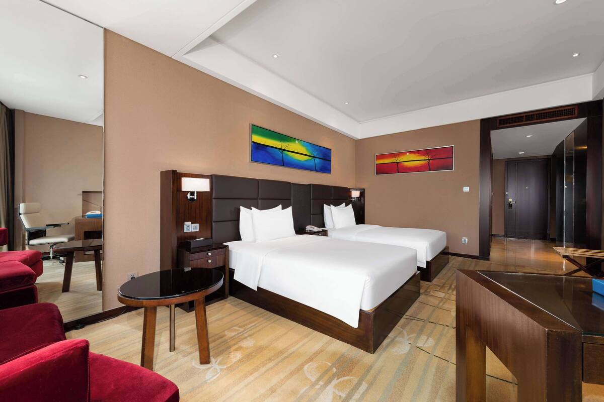 Una habitación de hotel con una cama grande, un escritorio, una silla y dos cuadros en la pared.