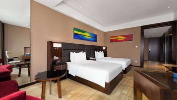 A hotel room with a large bed, a desk, a chair, and two paintings on the wall.
