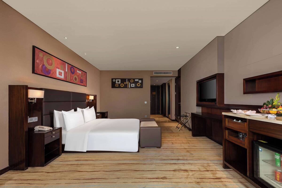 Una habitación de hotel con cama, mesitas de noche, televisor, escritorio y minibar.