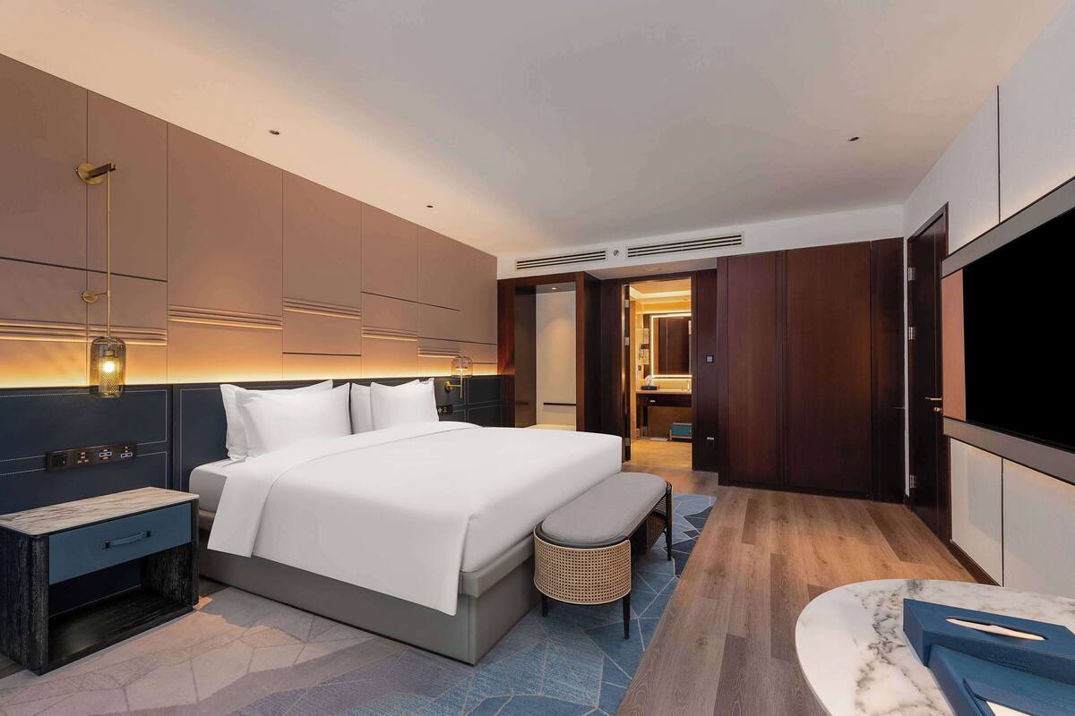 Una habitación de hotel moderna con una cama grande, mesitas de noche, un televisor y un baño visible a través de una puerta abierta.