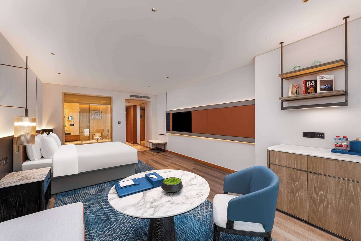 Habitación de hotel moderna con cama, escritorio, silla, mesita y televisor montado en la pared.