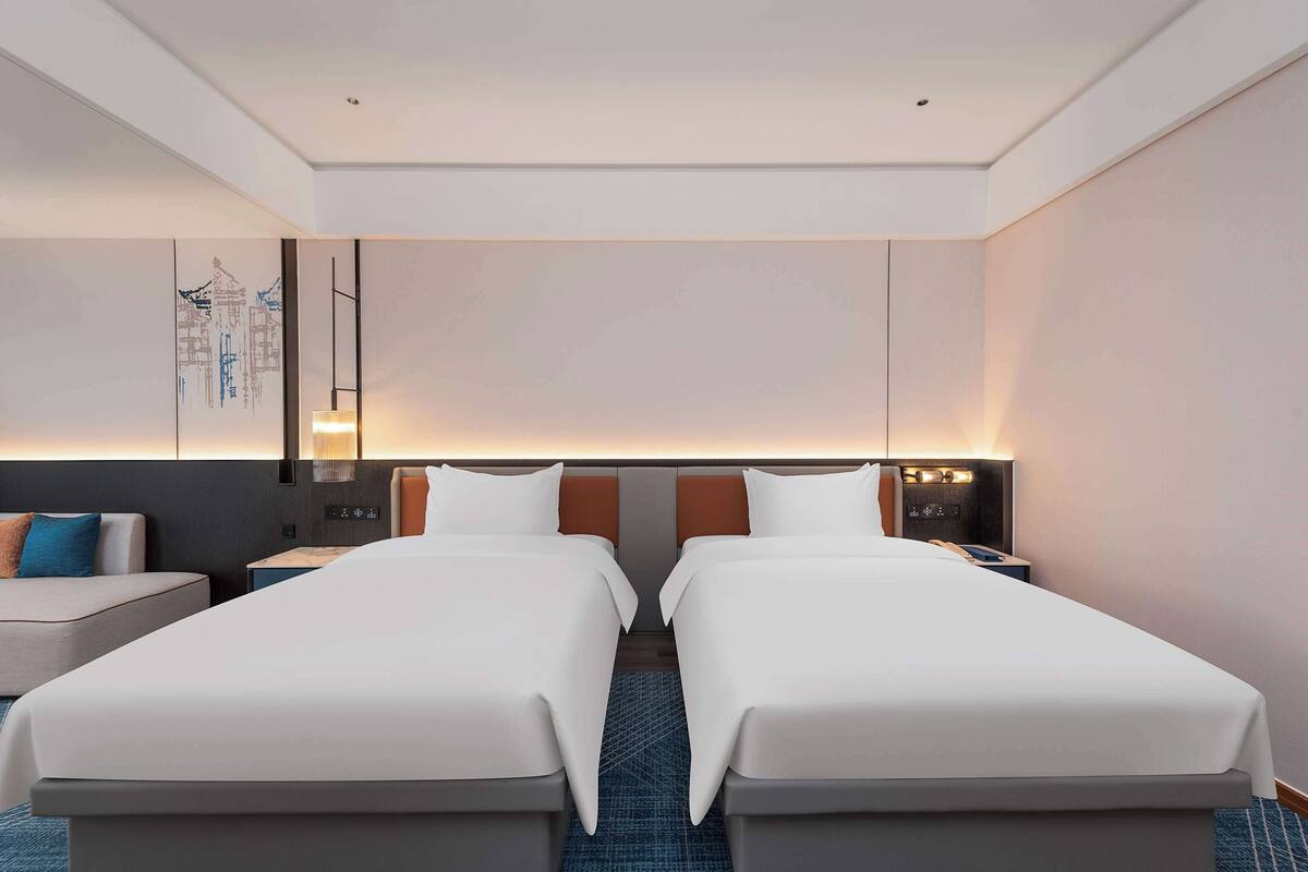 Habitación de hotel con dos camas, un sofá, un escritorio y una obra de arte colgada en la pared.