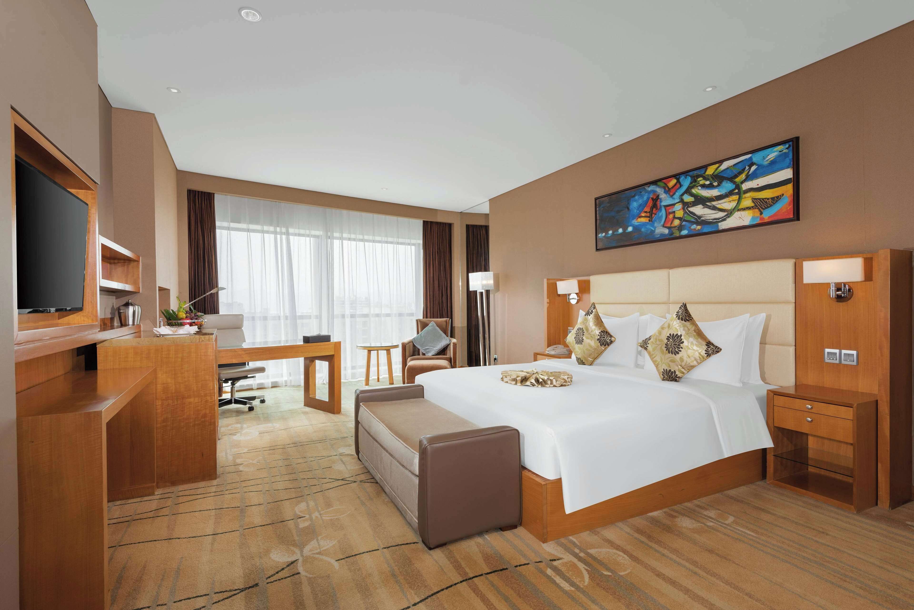 A hotel room with a large bed, a desk, a chair, a TV, and a painting on the wall.