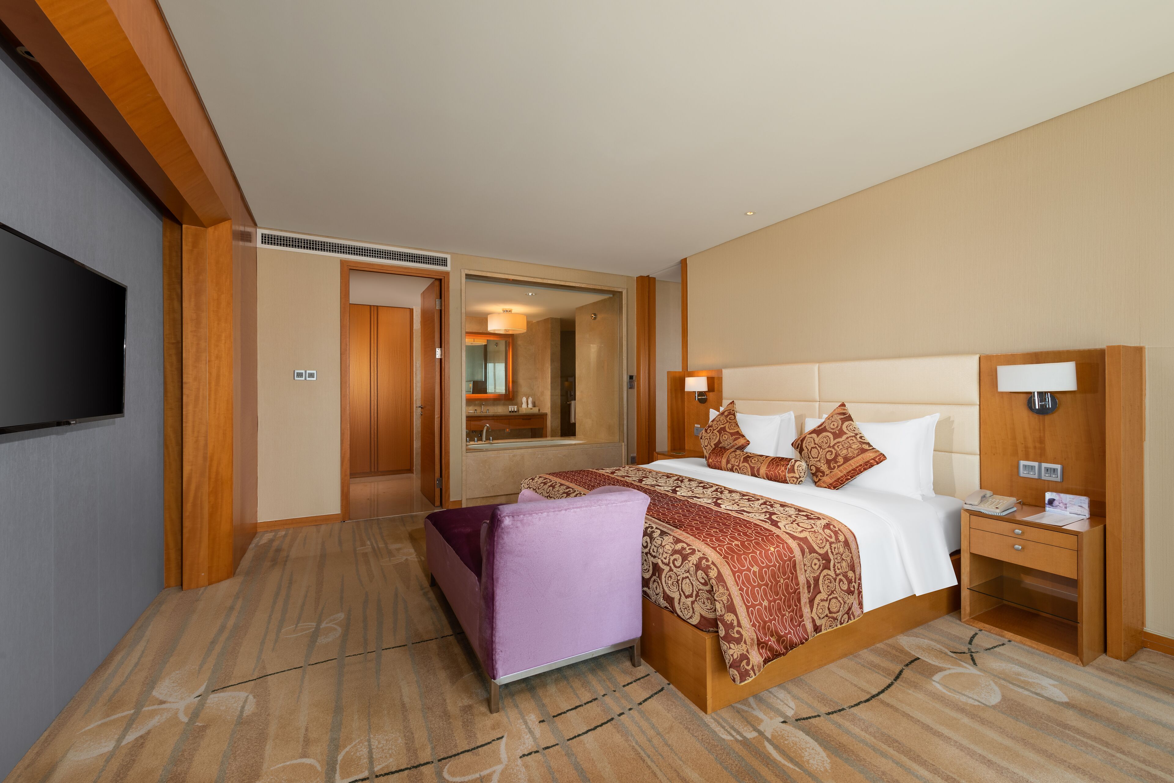 A hotel room with a large bed, a television, a desk with a lamp, and a bathroom visible through an open door.