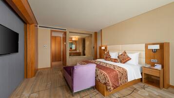 A hotel room with a large bed, a television, a desk with a lamp, and a bathroom visible through an open door.