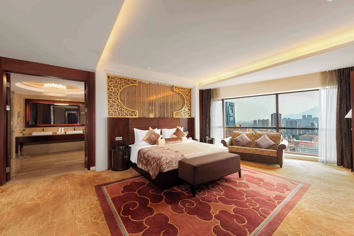 Habitación de hotel con una cama grande, un sofá, un televisor y vistas a la ciudad.