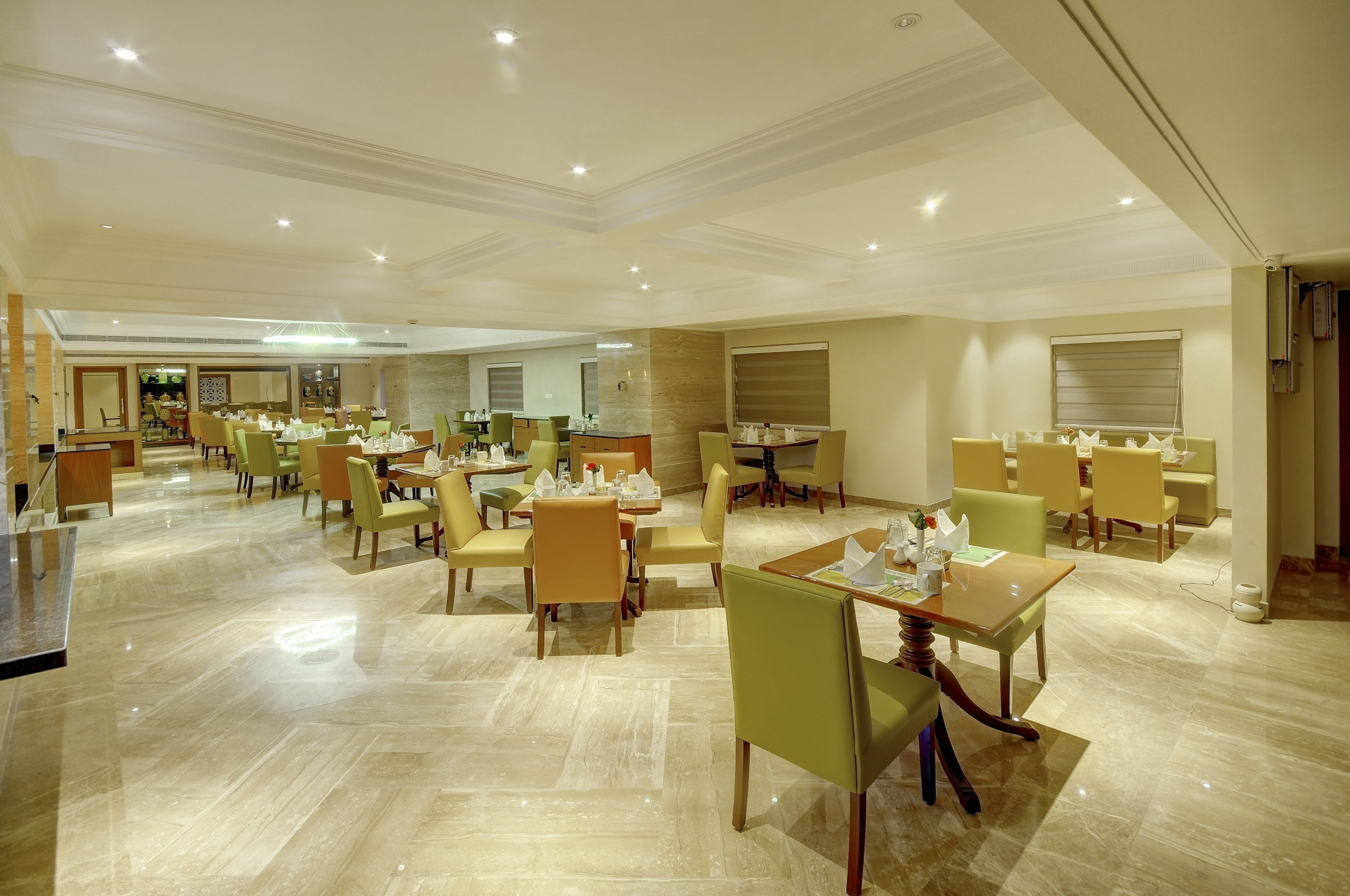A spacious hotel dining area with multiple tables and chairs, a polished marble floor, and a modern ceiling design.