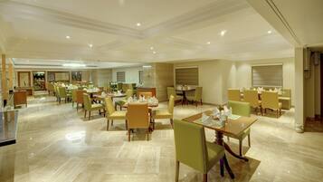 A spacious hotel dining area with multiple tables and chairs, a polished marble floor, and a modern ceiling design.