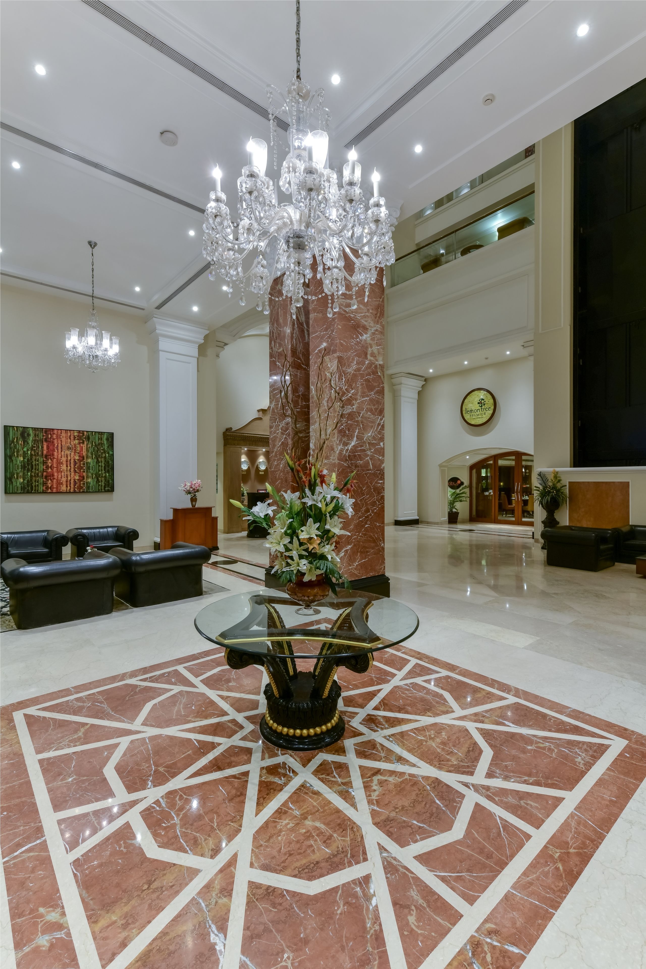 A spacious lobby with a large chandelier, marble flooring, leather seating, and a reception desk.