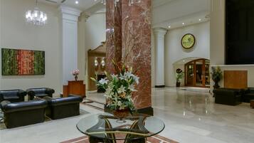 A spacious lobby with a large chandelier, marble flooring, leather seating, and a reception desk.