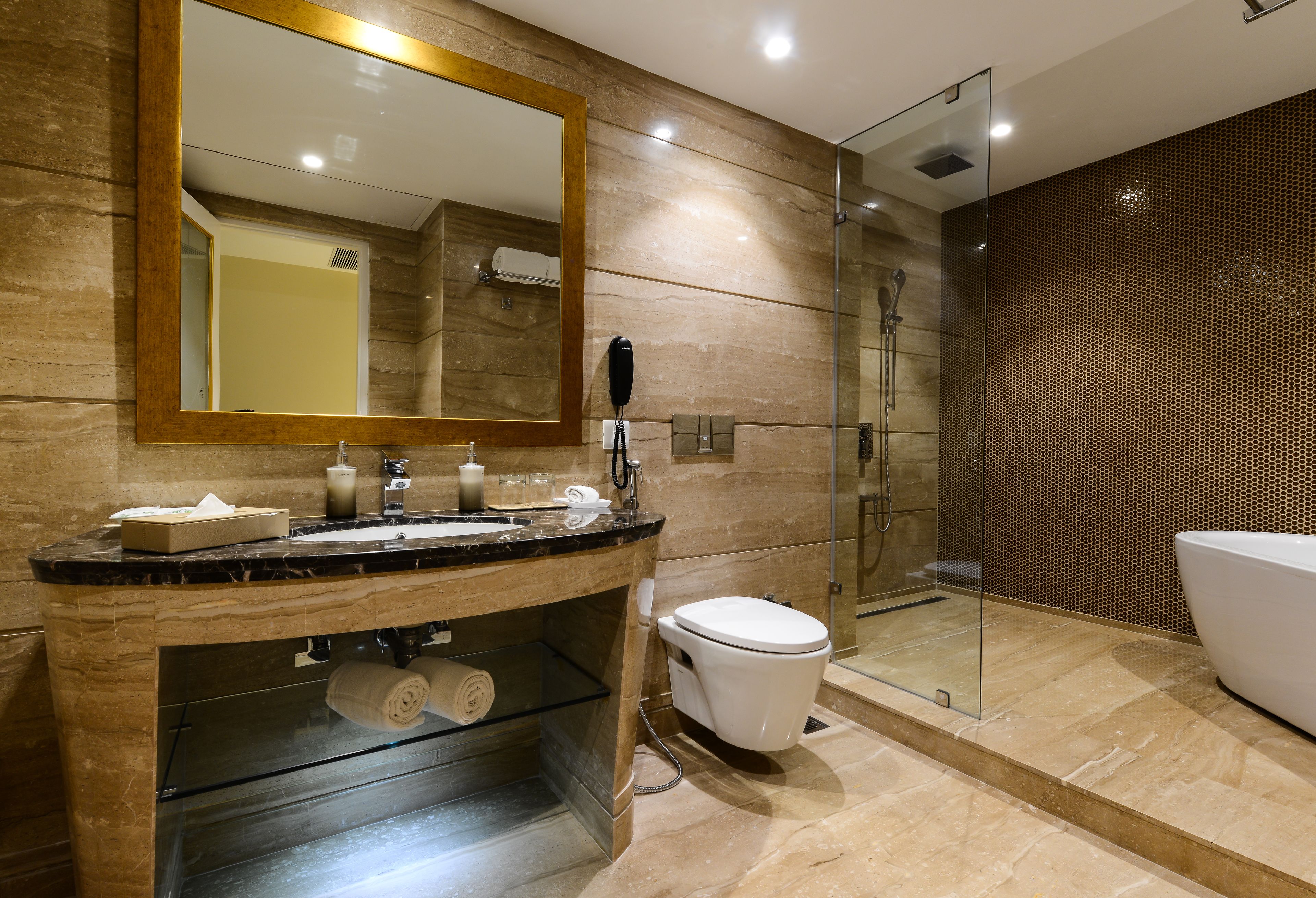 A modern bathroom with a marble sink, a large mirror, a toilet, and a glass-enclosed shower.