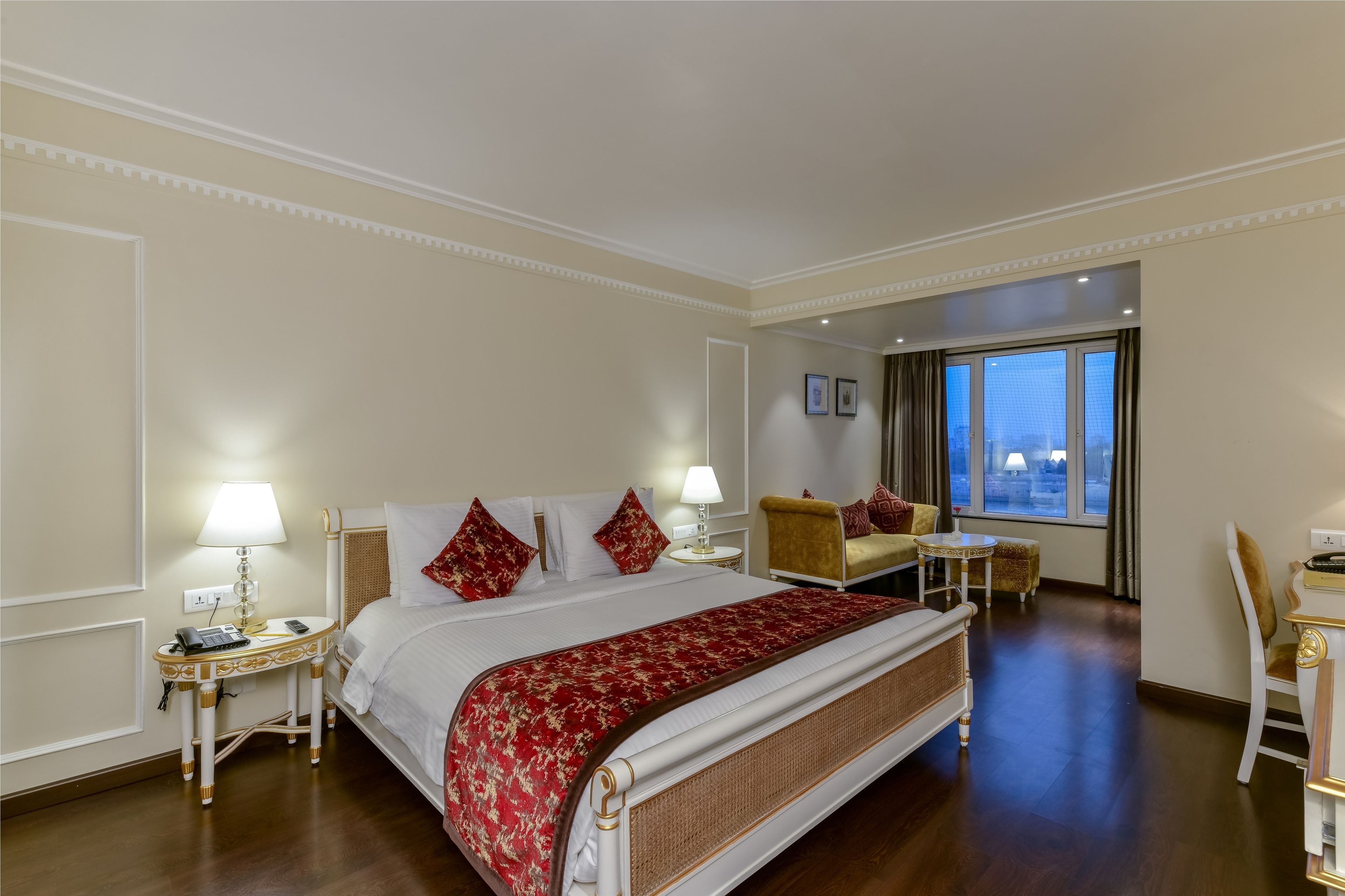 Een hotelkamer met een groot bed, een bureau, een stoel en uitzicht op de stad door een groot raam.