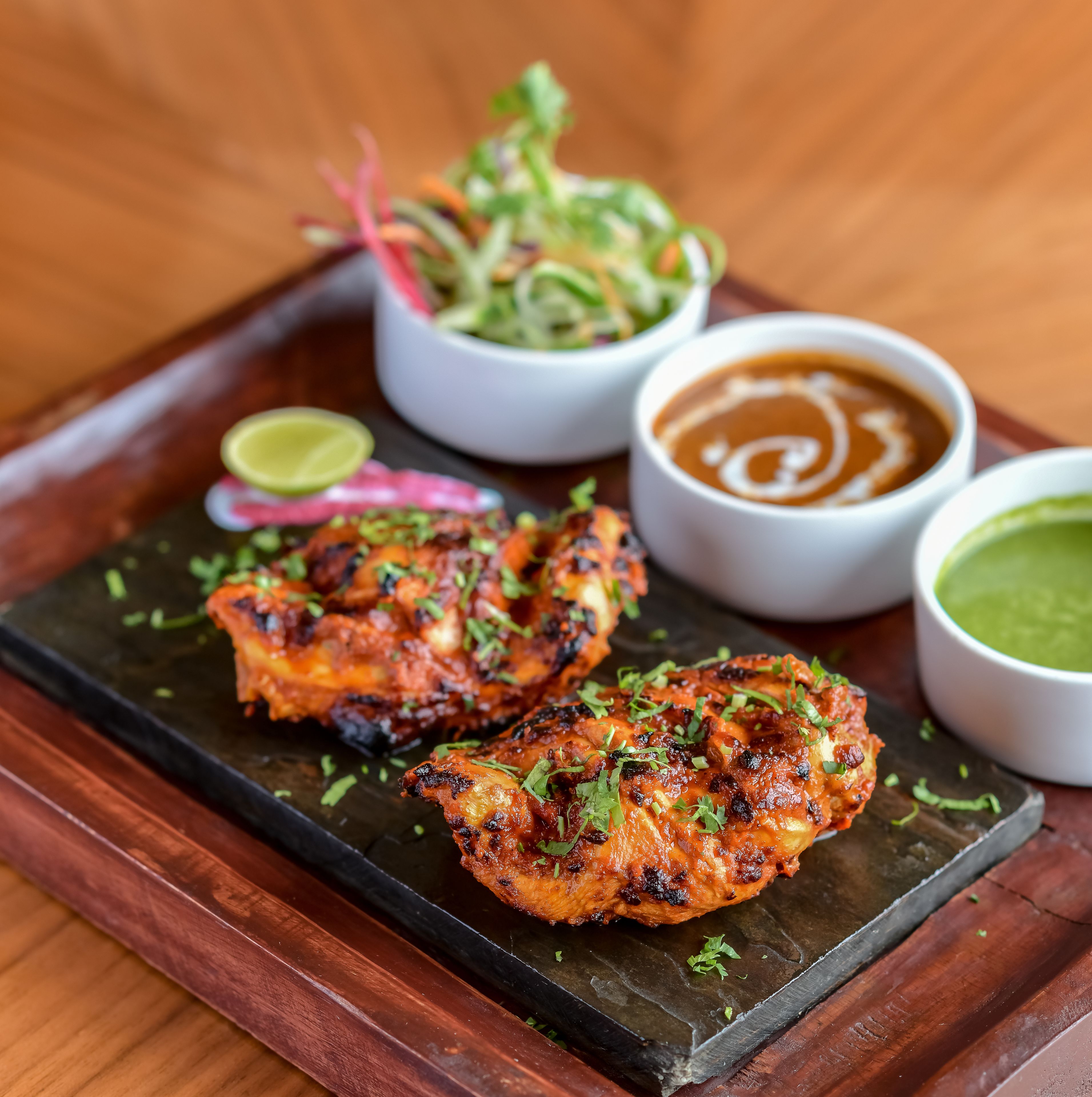 Grilled chicken wings with various sauces and a lime wedge on a slate serving tray.
