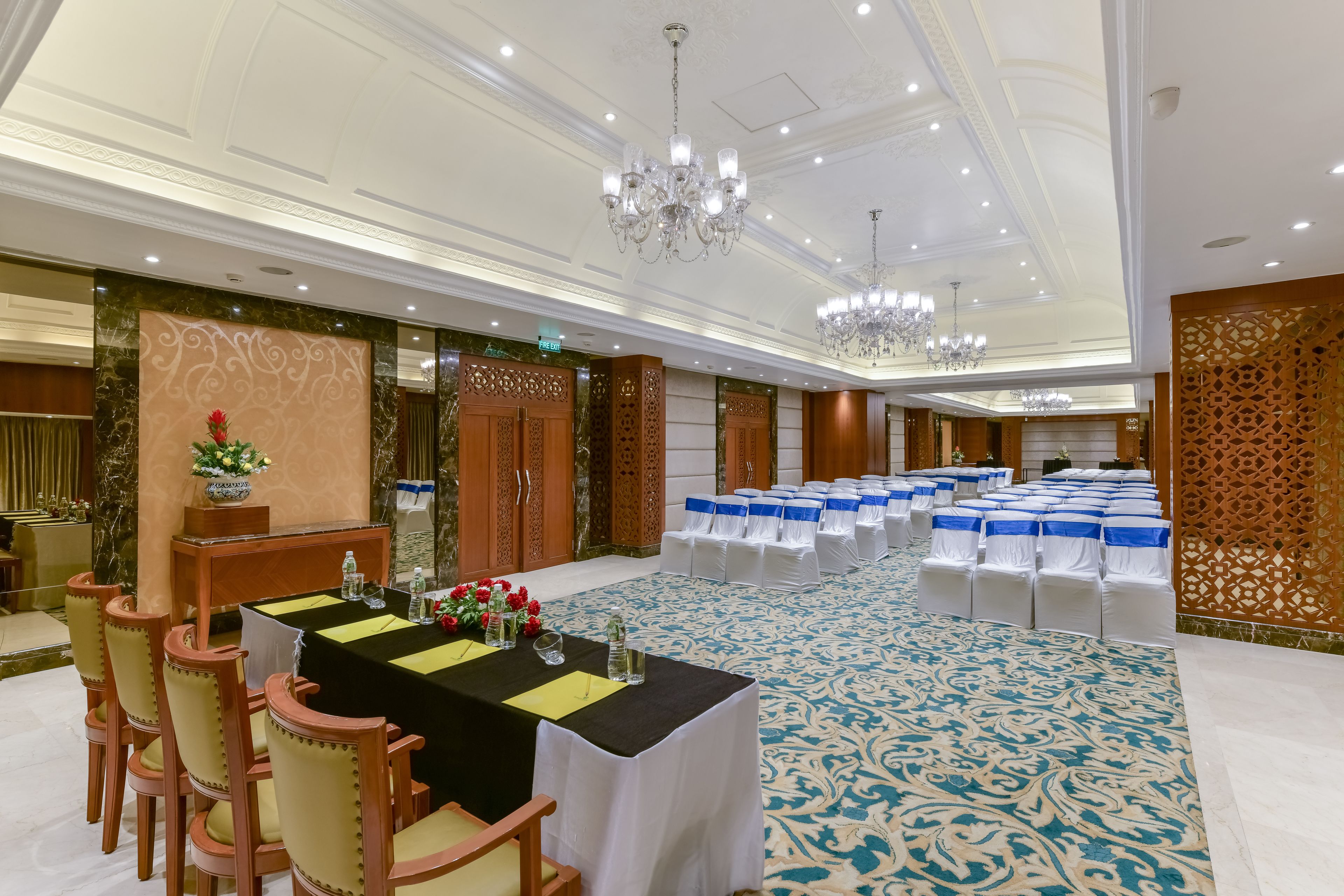 A banquet hall with a long table set for a meeting, surrounded by chairs, and a patterned carpet.