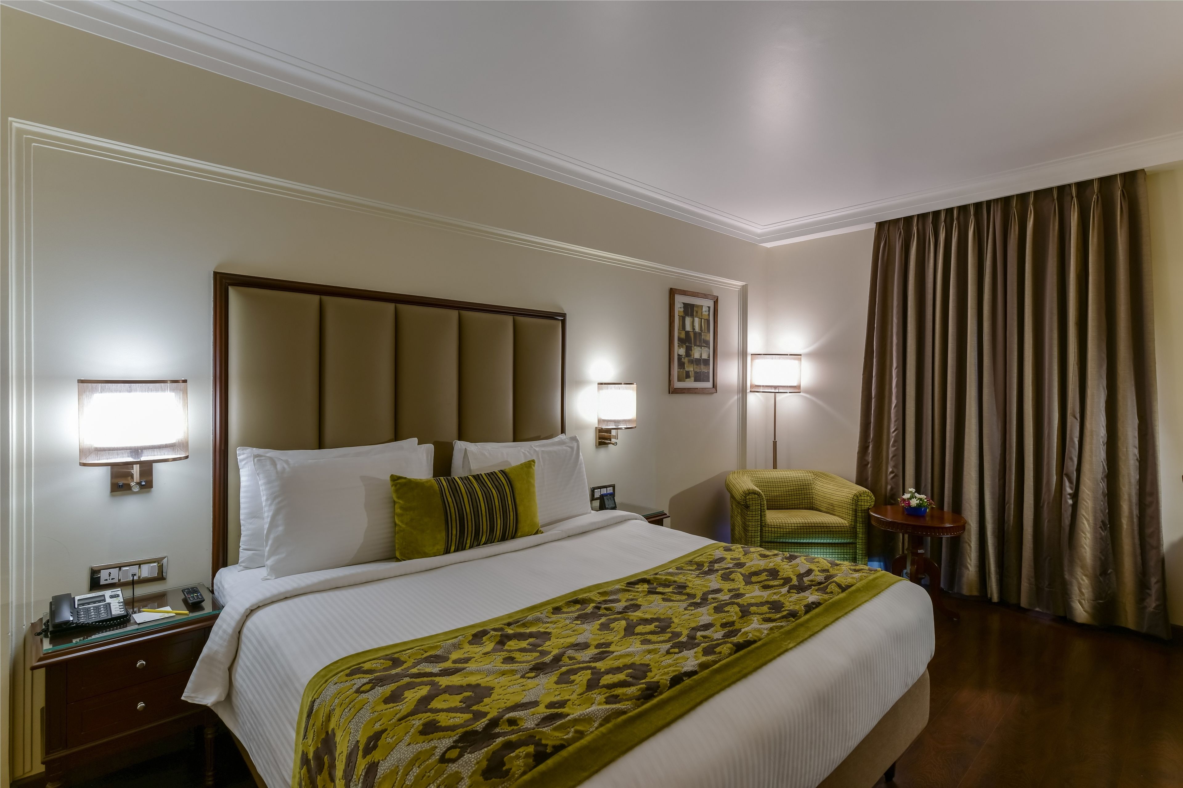Une chambre d’hôtel avec un grand lit, des lampes de chevet, un téléphone, une petite table avec une lampe et une chaise.