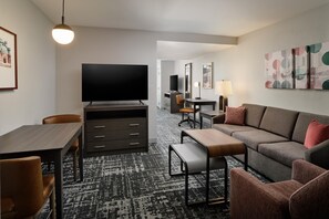 A hotel room with a flat-screen TV, a desk with a chair, a sofa, and a patterned carpet. - Homewood Suites by Hilton Columbus/OSU, OH (Columbus)