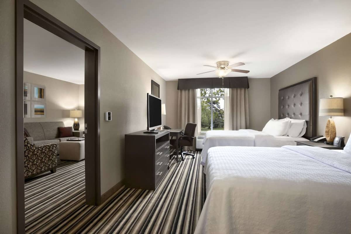 A hotel room with a bed, a desk with a computer, a television, a chair, and a window with curtains.