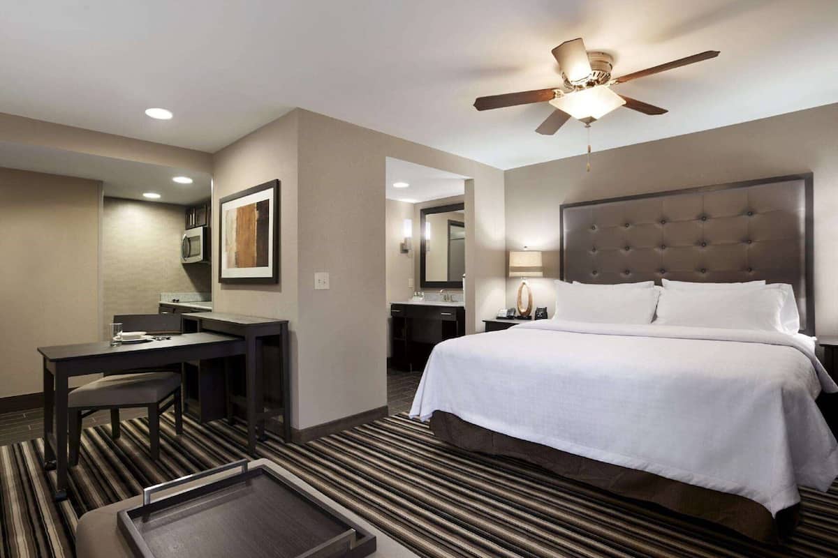 A hotel room with a bed, desk, chair, and a ceiling fan.