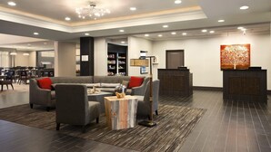A modern lobby with a sofa, chairs, a coffee table, a reception desk, and a bookshelf. - Homewood Suites by Hilton Columbus/OSU, OH (Columbus)