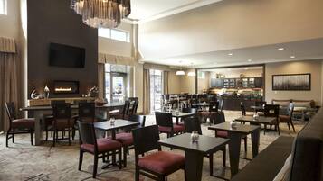 A hotel lobby with multiple seating areas, a fireplace, a television, and a kitchen in the background.