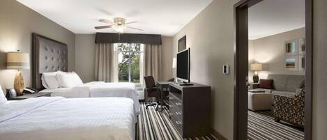 A hotel room with two beds, a desk, a TV, and a view of the outdoors.