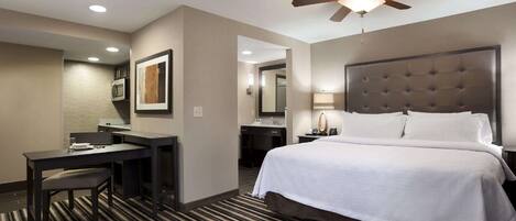 A hotel room with a bed, desk, chair, and a ceiling fan.