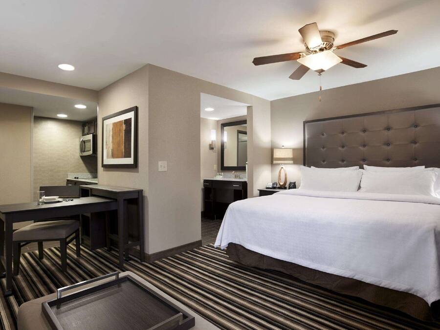 Quarto de hotel com cama, escrivaninha, cadeira e ventilador de teto.