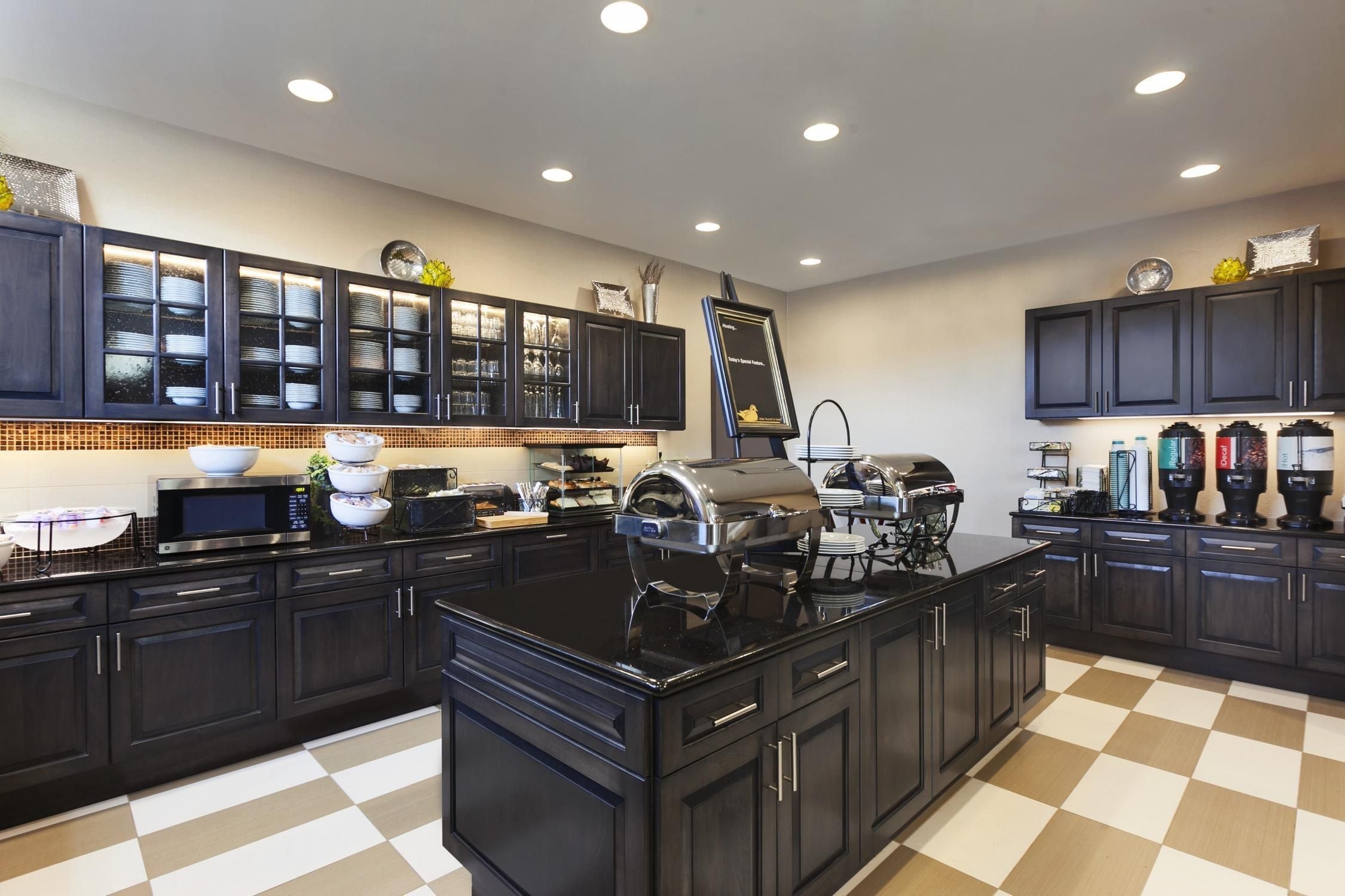 A modern kitchen with dark cabinetry, a central island, a microwave, a grill, and a checkered floor.