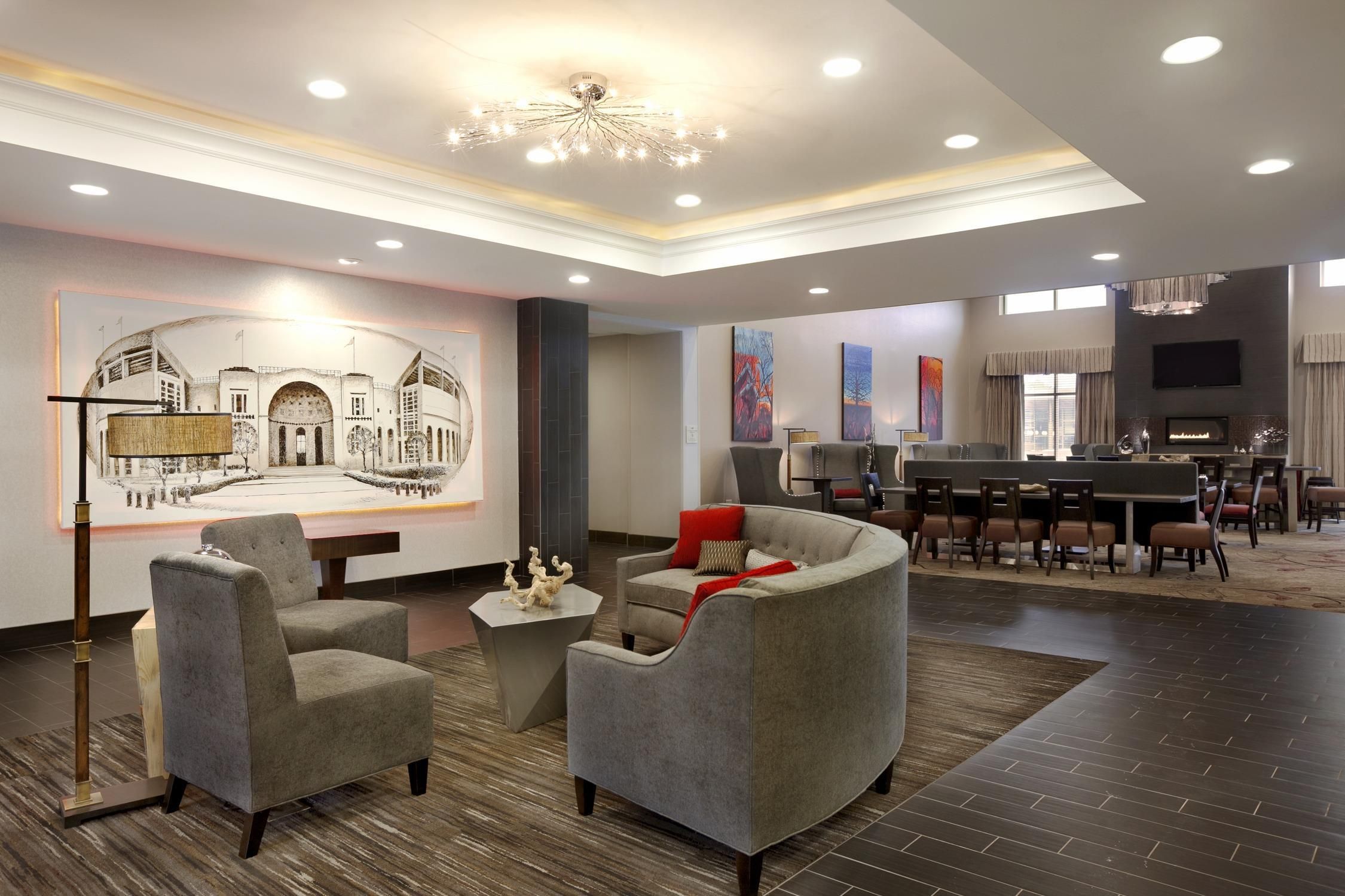 A hotel lobby with a dining area, seating arrangements, and a large artwork on the wall.