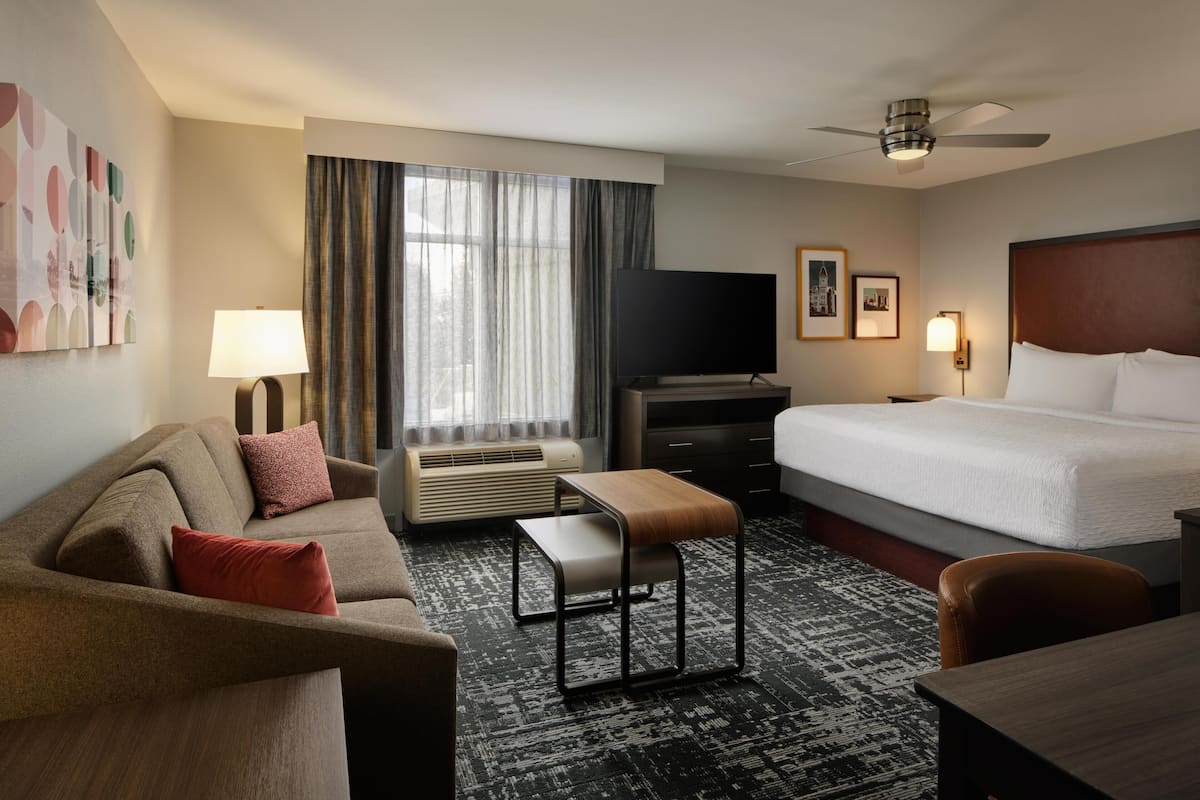 A hotel room with a bed, a sofa, a TV, a desk, and a window with curtains.