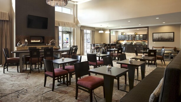 A hotel lobby with multiple seating areas, a fireplace, a television, and a kitchen in the background. - Homewood Suites by Hilton Columbus/OSU, OH (Columbus)