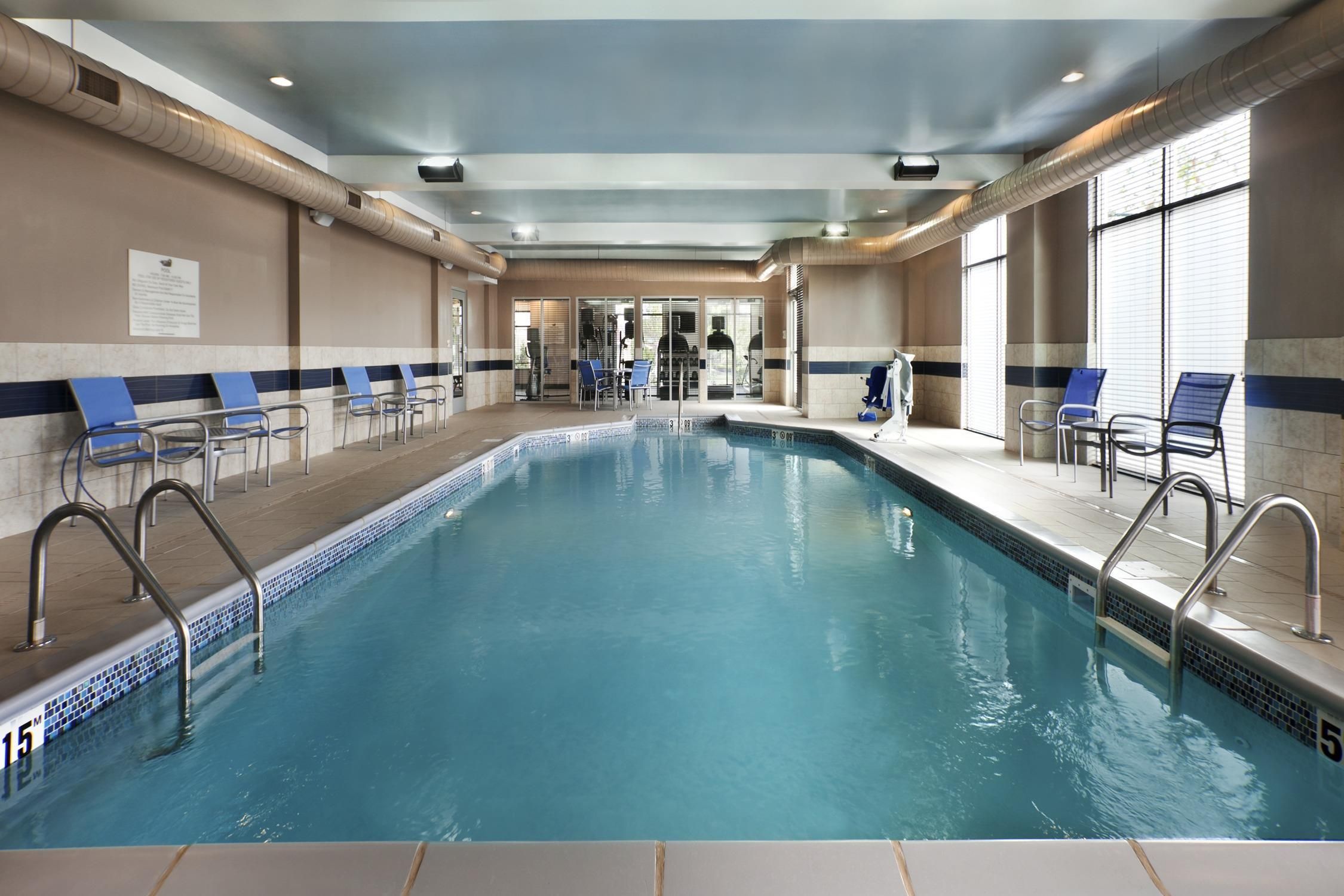 An indoor swimming pool with clear water, surrounded by lounge chairs and a tiled floor.
