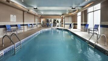 An indoor swimming pool with clear water, surrounded by lounge chairs and a tiled floor.