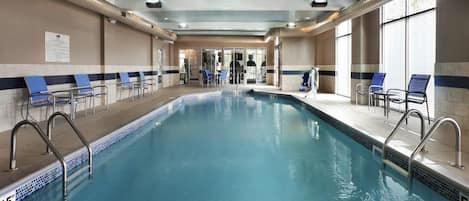 Ein überdachter Pool mit klarem Wasser, umgeben von Liegestühlen und einem gefliesten Boden.