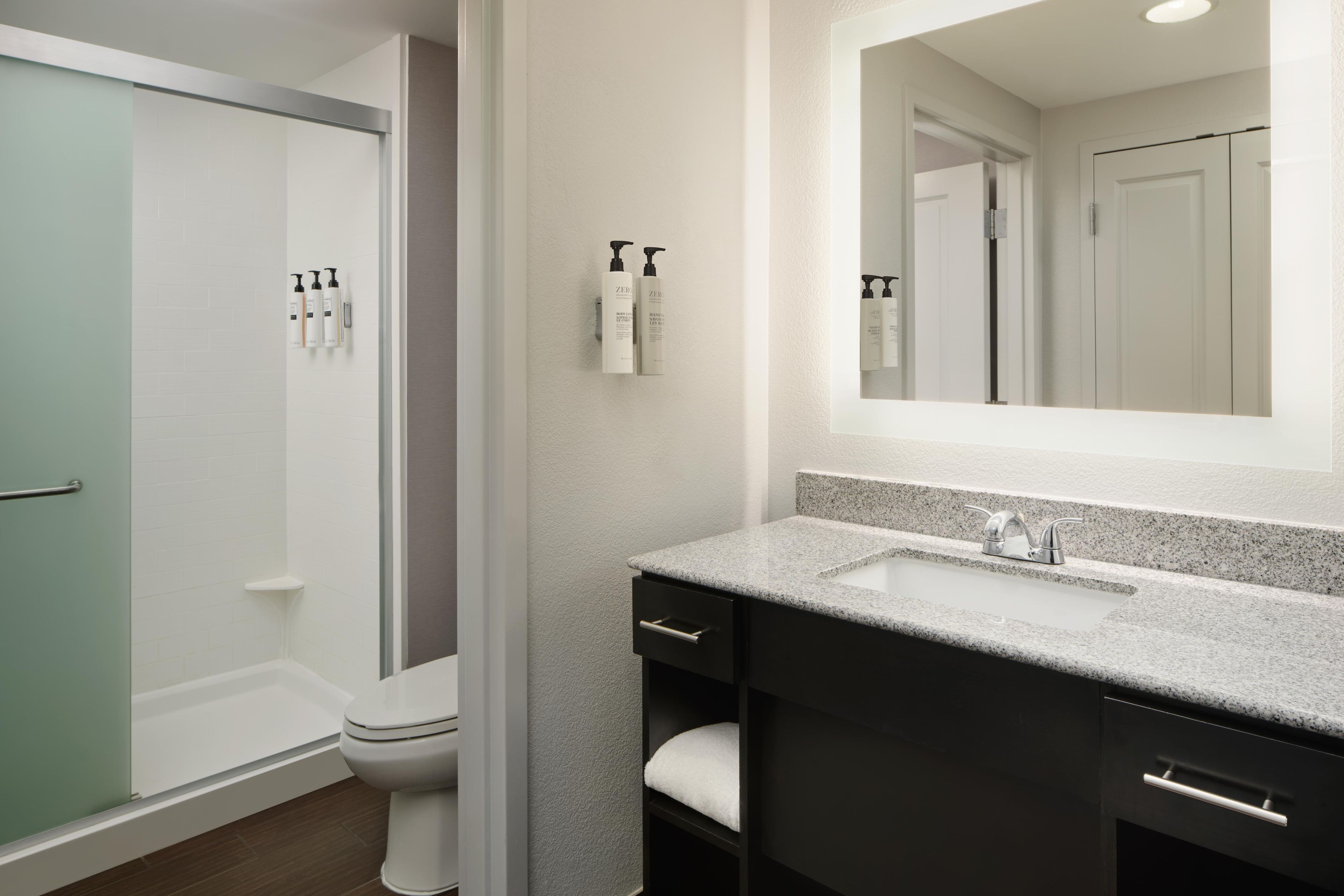 Une salle de bain moderne avec une douche à l’italienne, des toilettes, un lavabo doté d’un plan de travail en granit et un miroir au-dessus du lavabo.
