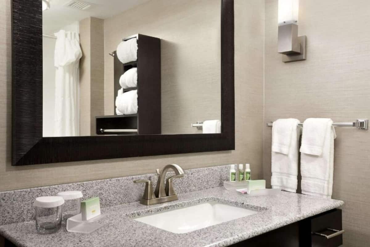 A modern bathroom with a large mirror, a granite countertop, a sink, and a towel rack.