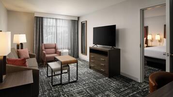 A hotel room with a sofa, armchair, TV, and a bed.