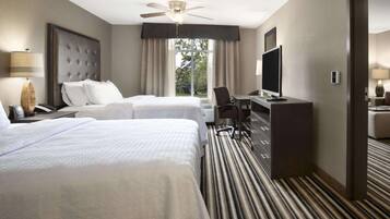 A hotel room with two beds, a desk, a television, and a ceiling fan.