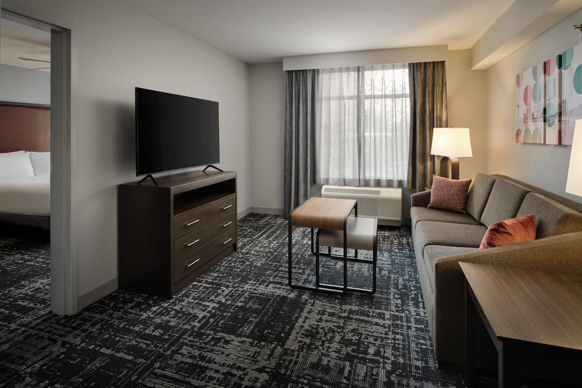 A hotel room with a bed, a TV, a desk, a sofa, and a window with curtains.