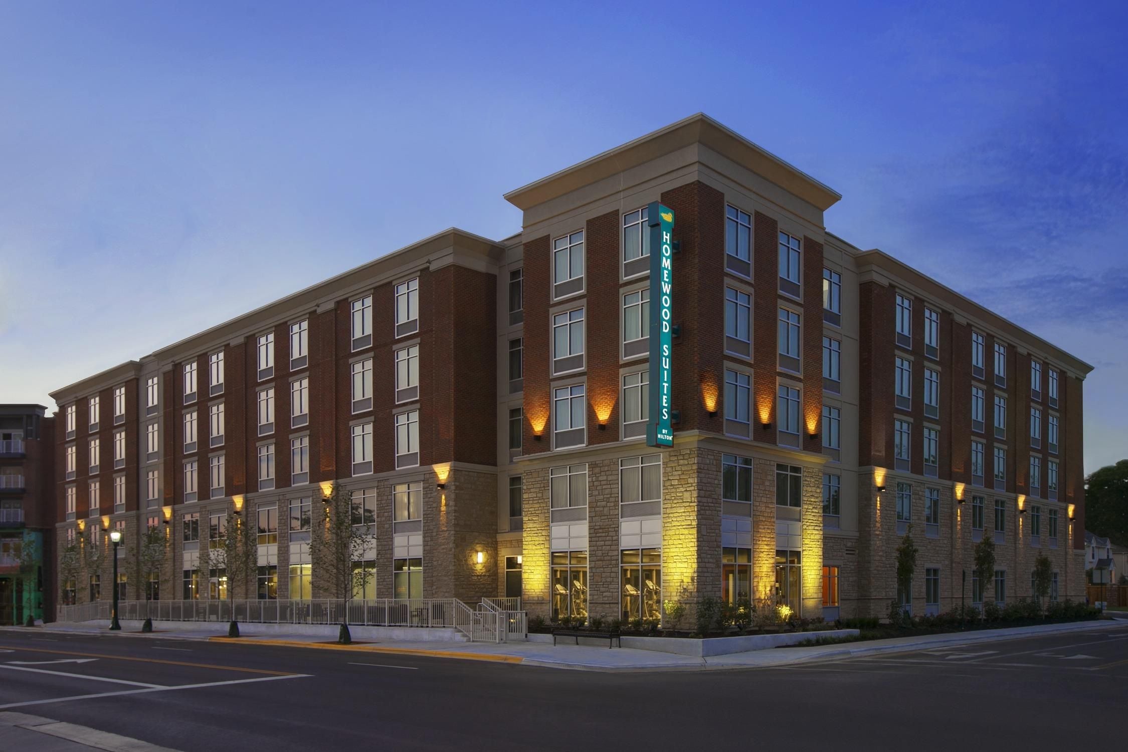 A multi-story hotel with a brick facade, large windows, and a prominent sign indicating it is a Homewood Suites.